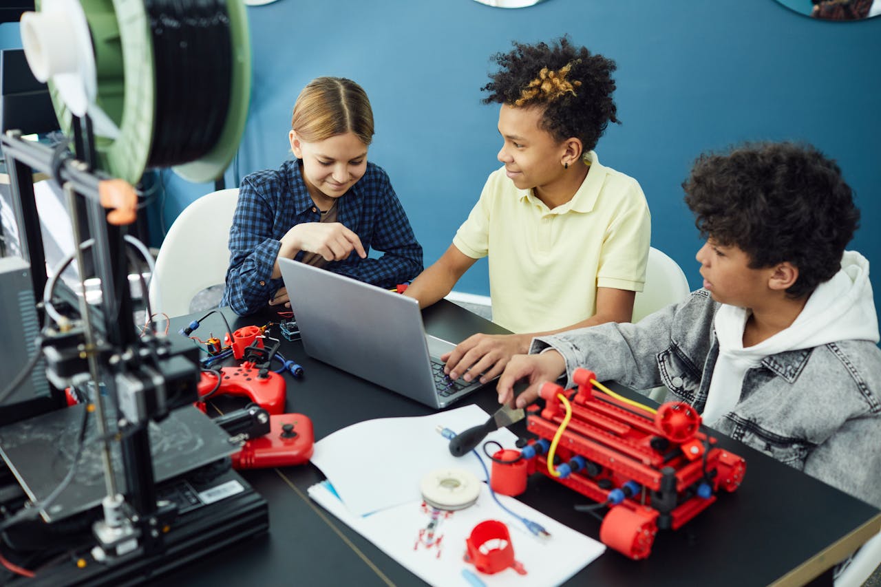Group of diverse kids collaborating on a 3D printing project using a laptop and other devices.